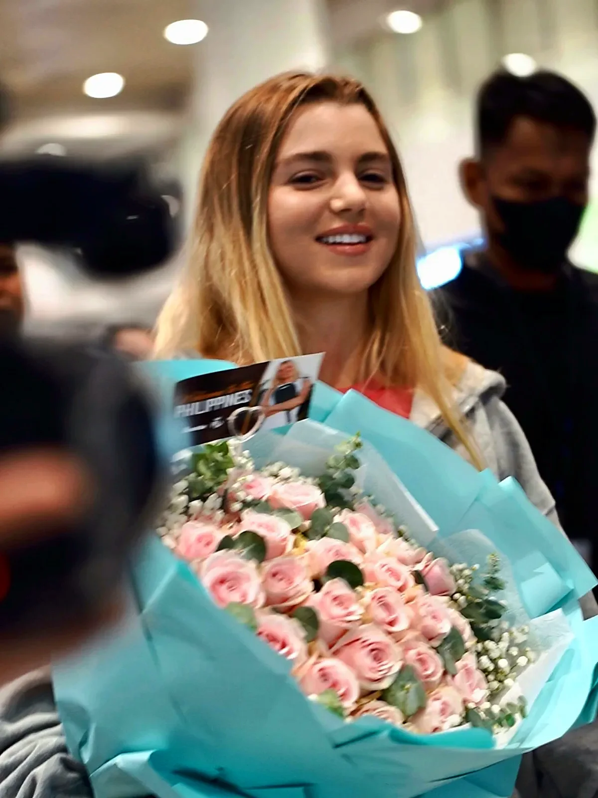 Anna Leigh Waters smiles with a bouquet of pink roses at NAIA