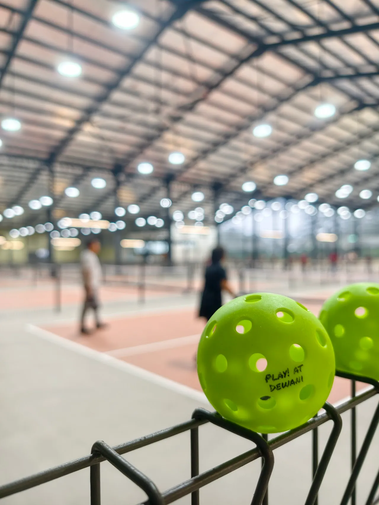 Branded pickleballs on the fence at Play! at Dewani, with the courts behind